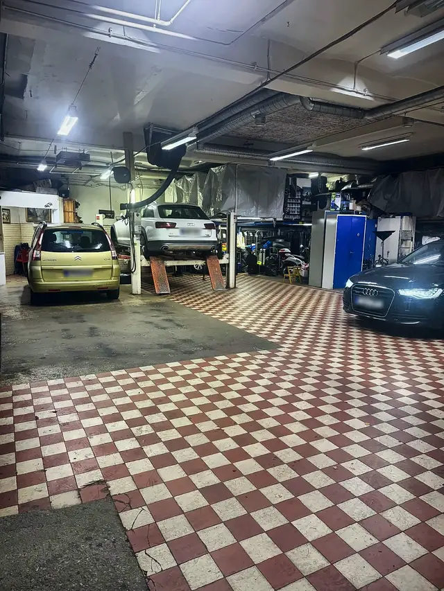 Verkstadshallen med fyrpelarlyft, en Audi A6 på lyften och rött och vitt rutigt klinkergolv